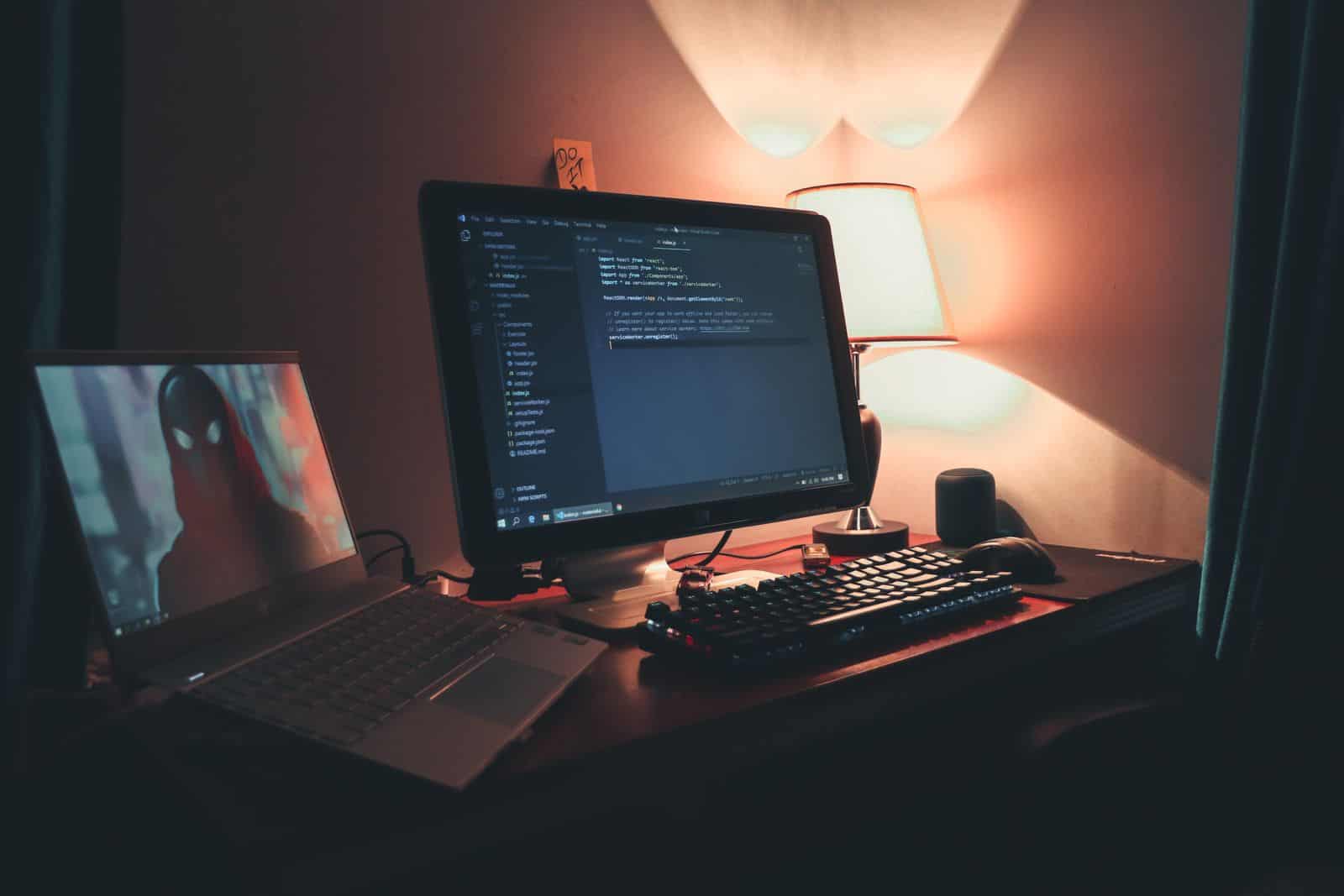 A web developer's desk with a monitor running Visual Studio Code and a laptop as a second screen