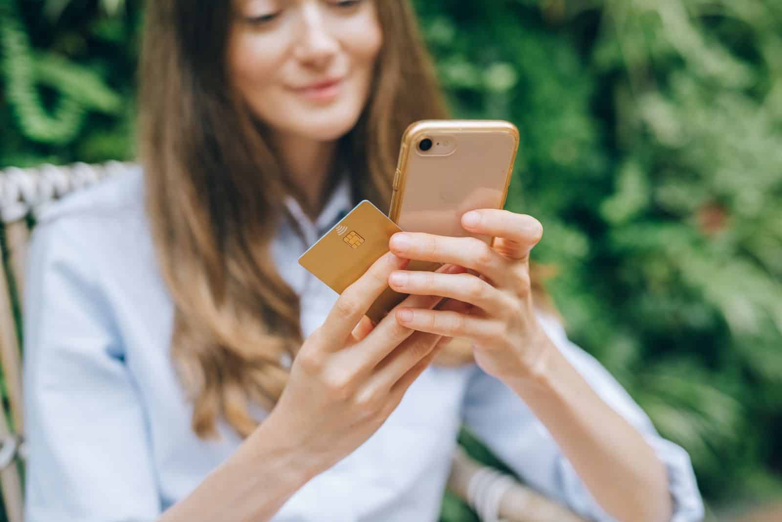 A person holding a smartphone and a contactless bank card while shopping online