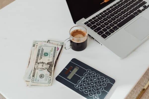 Laptop, US dollar bills and a calculator on a desk representing web project pricing and budgeting
